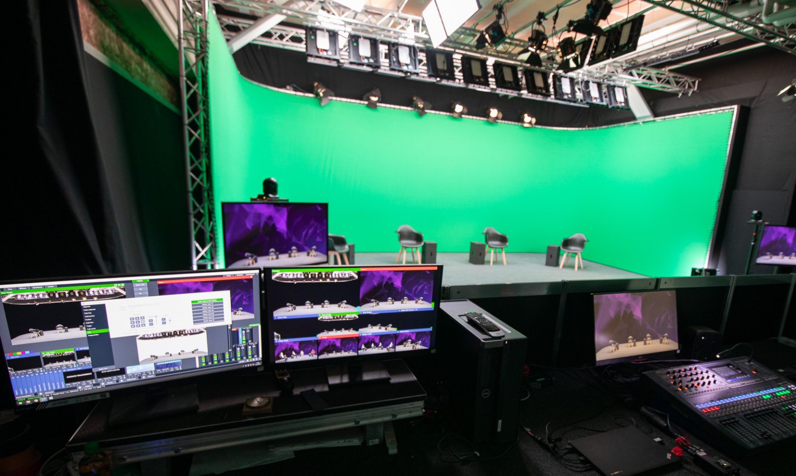 Streamingstudio mit großer Greenscreen-Wand, Scheinwerferzeile und Regiepult mit mehreren Kontrollmonitoren